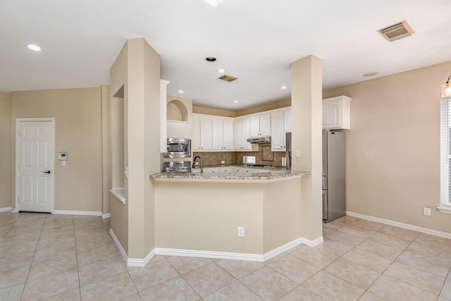 kitchen with kitchen peninsula, decorative backsplash, light stone countertops, appliances with stainless steel finishes, and white cabinetry