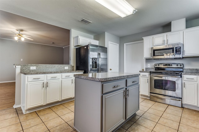 kitchen with appliances with stainless steel finishes, light tile patterned floors, a kitchen island, and white cabinets