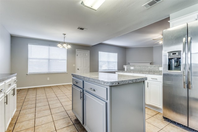 kitchen featuring stainless steel refrigerator with ice dispenser, white cabinetry, decorative light fixtures, light tile patterned floors, and a kitchen island