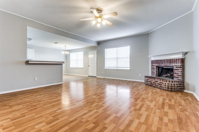 unfurnished living room with ceiling fan with notable chandelier, crown molding, light hardwood / wood-style floors, and a brick fireplace