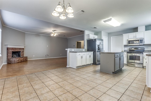 kitchen featuring white cabinetry, hanging light fixtures, stainless steel appliances, a center island, and ceiling fan with notable chandelier