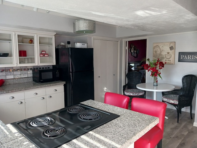 kitchen featuring tasteful backsplash, a textured ceiling, black appliances, hardwood / wood-style floors, and white cabinetry