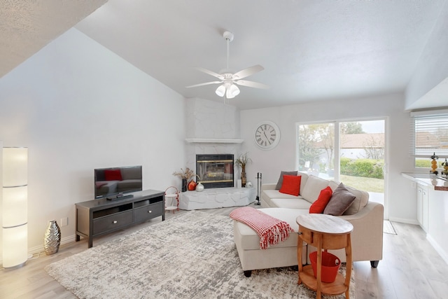 living room with ceiling fan, light wood-type flooring, a fireplace, and vaulted ceiling