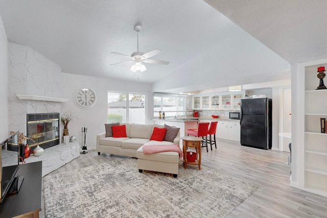 living room with light hardwood / wood-style floors, a stone fireplace, ceiling fan, and lofted ceiling