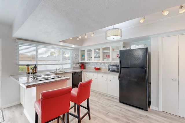 kitchen with backsplash, white cabinets, black appliances, and light wood-type flooring