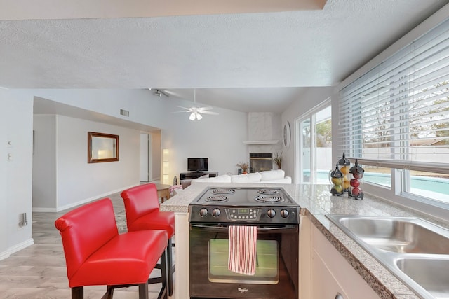 kitchen featuring a large fireplace, vaulted ceiling, light hardwood / wood-style flooring, white cabinetry, and black / electric stove