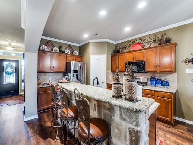 kitchen with a breakfast bar, dark hardwood / wood-style floors, decorative backsplash, an island with sink, and stainless steel appliances