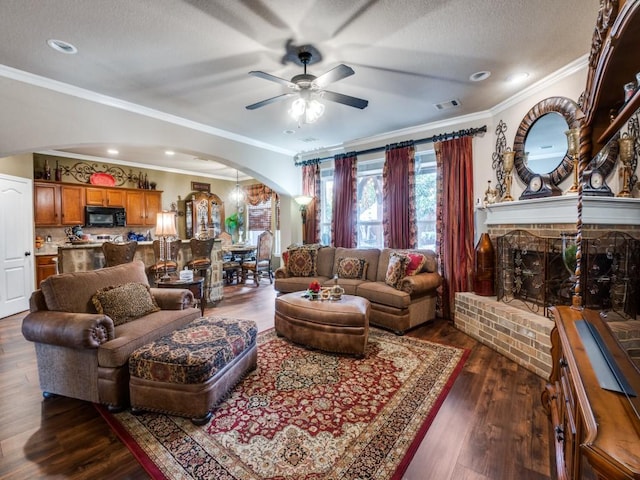 living room featuring ceiling fan, dark hardwood / wood-style floors, a textured ceiling, a fireplace, and ornamental molding