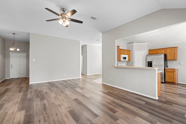 unfurnished living room featuring lofted ceiling, wood-type flooring, and ceiling fan with notable chandelier