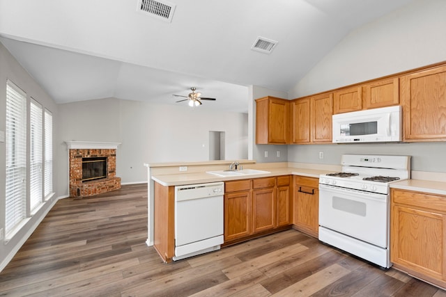 kitchen featuring white appliances, vaulted ceiling, dark wood-type flooring, sink, and a fireplace