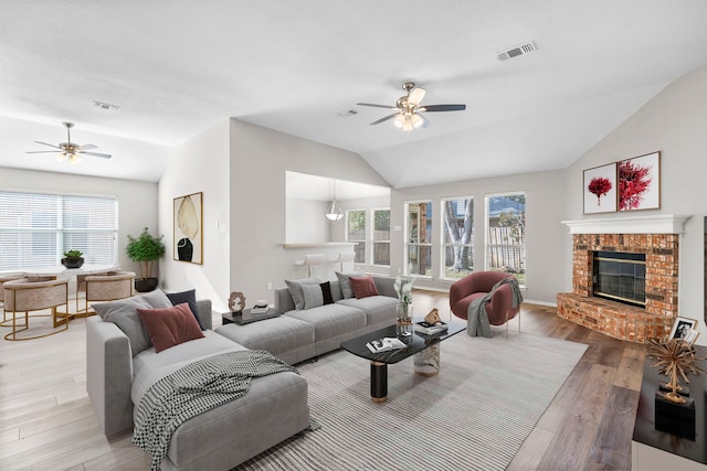 living room featuring ceiling fan, hardwood / wood-style floors, lofted ceiling, and a brick fireplace