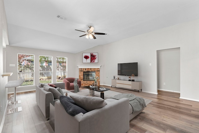 living room featuring a fireplace, light hardwood / wood-style floors, vaulted ceiling, and ceiling fan