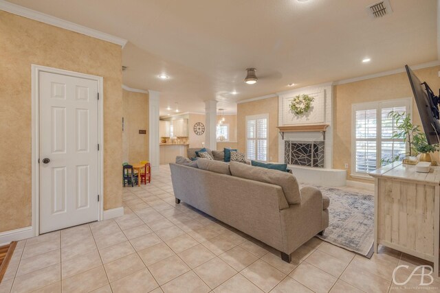 tiled living room with ceiling fan, a large fireplace, and ornamental molding