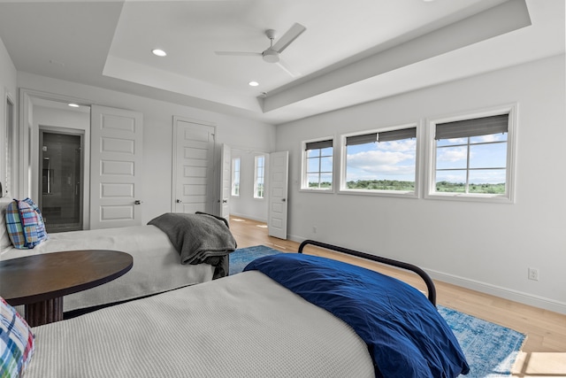 bedroom featuring light wood-type flooring, a tray ceiling, and ceiling fan