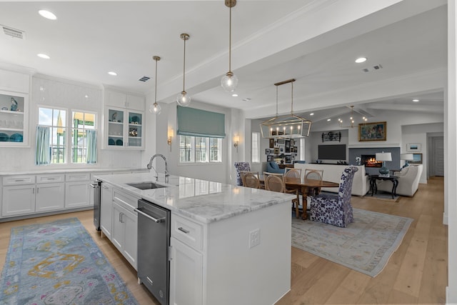 kitchen with white cabinetry, sink, light stone countertops, light hardwood / wood-style flooring, and a center island with sink