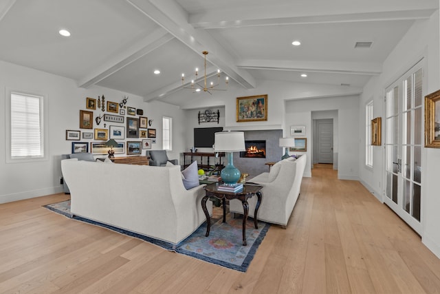 living room featuring a fireplace, vaulted ceiling with beams, light hardwood / wood-style flooring, and a notable chandelier