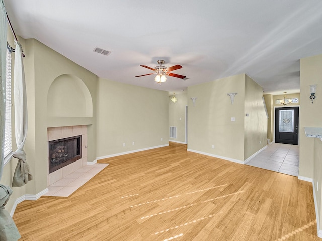 unfurnished living room featuring ceiling fan with notable chandelier, a fireplace, and light wood-type flooring