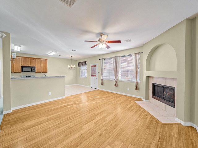 unfurnished living room featuring ceiling fan with notable chandelier, a fireplace, and light hardwood / wood-style floors