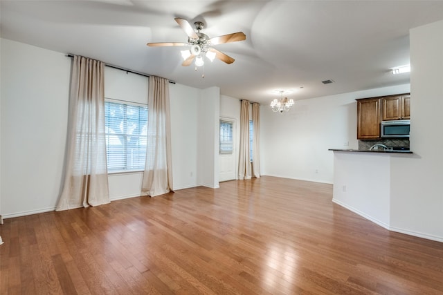 unfurnished living room featuring ceiling fan with notable chandelier and light hardwood / wood-style floors