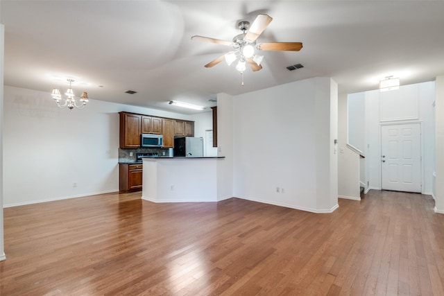 unfurnished living room featuring ceiling fan with notable chandelier and light wood-type flooring