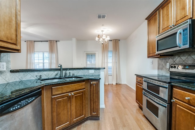 kitchen with dark stone counters, an inviting chandelier, sink, light wood-type flooring, and stainless steel appliances