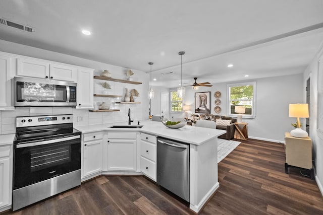 kitchen with kitchen peninsula, stainless steel appliances, dark wood-type flooring, sink, and white cabinetry