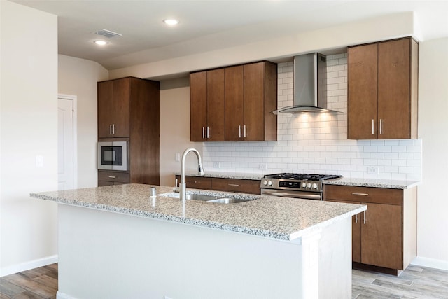 kitchen with high end stainless steel range, an island with sink, wall chimney range hood, and sink