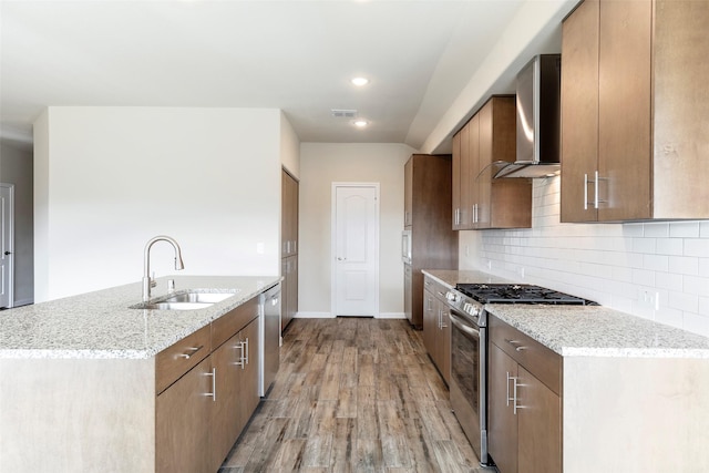 kitchen with sink, light hardwood / wood-style flooring, wall chimney exhaust hood, decorative backsplash, and stainless steel appliances