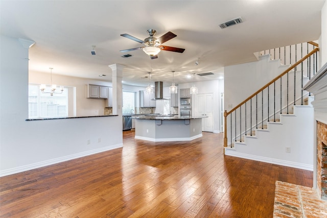 unfurnished living room with ornate columns, ceiling fan with notable chandelier, and dark hardwood / wood-style flooring