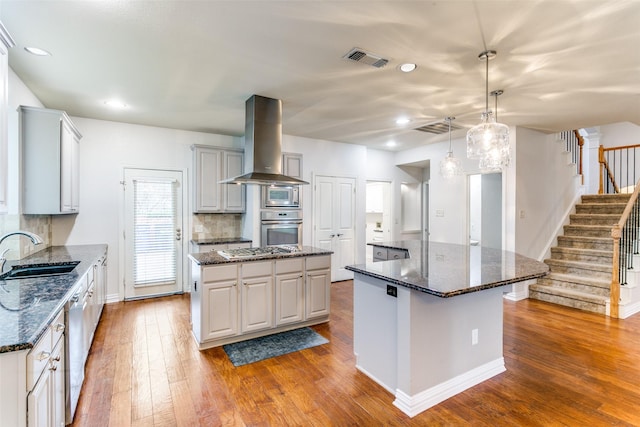 kitchen with sink, appliances with stainless steel finishes, island range hood, a kitchen island, and dark stone counters