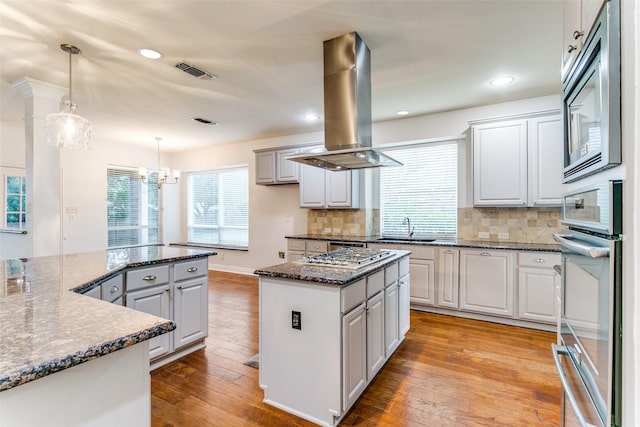 kitchen featuring a kitchen island, appliances with stainless steel finishes, island range hood, decorative light fixtures, and dark stone counters