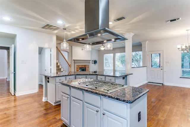 kitchen with pendant lighting, a center island, island range hood, white cabinets, and stainless steel gas stovetop