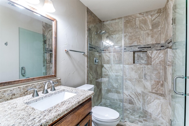 bathroom featuring a shower with door, vanity, and toilet