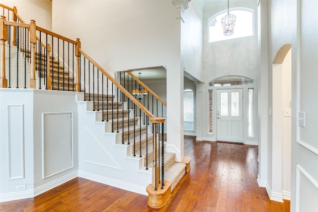 foyer entrance featuring hardwood / wood-style flooring, a notable chandelier, ornate columns, and a high ceiling