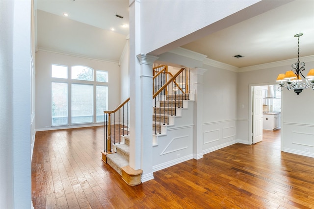 stairs with crown molding, wood-type flooring, decorative columns, and a wealth of natural light