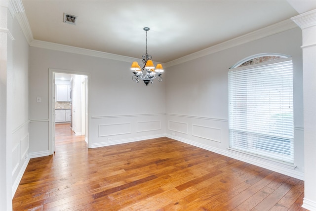 empty room with hardwood / wood-style flooring, ornamental molding, and a notable chandelier