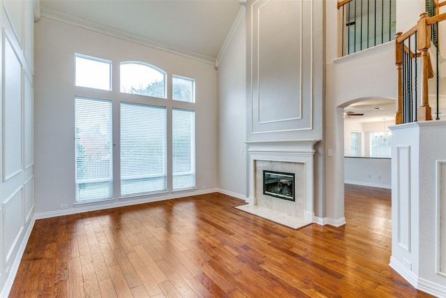 unfurnished living room with hardwood / wood-style flooring, a fireplace, a high ceiling, and crown molding