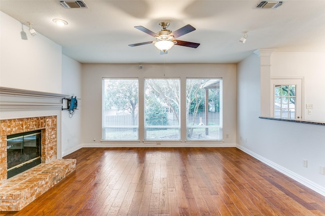 unfurnished living room featuring wood-type flooring, plenty of natural light, and a brick fireplace