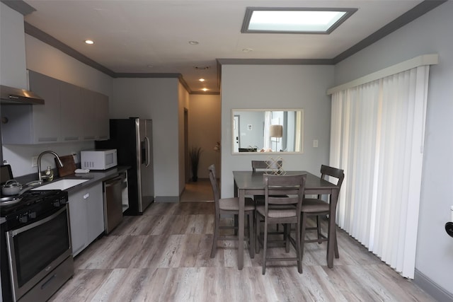 kitchen featuring gray cabinetry, wall chimney range hood, sink, light hardwood / wood-style flooring, and appliances with stainless steel finishes