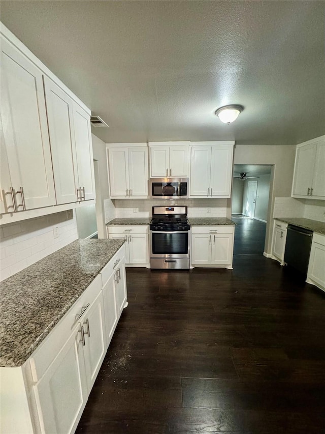 kitchen with dark stone countertops, appliances with stainless steel finishes, dark hardwood / wood-style flooring, decorative backsplash, and white cabinets