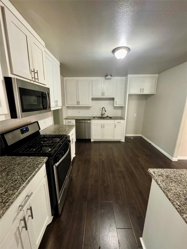 kitchen featuring sink, appliances with stainless steel finishes, dark stone countertops, white cabinets, and dark hardwood / wood-style flooring