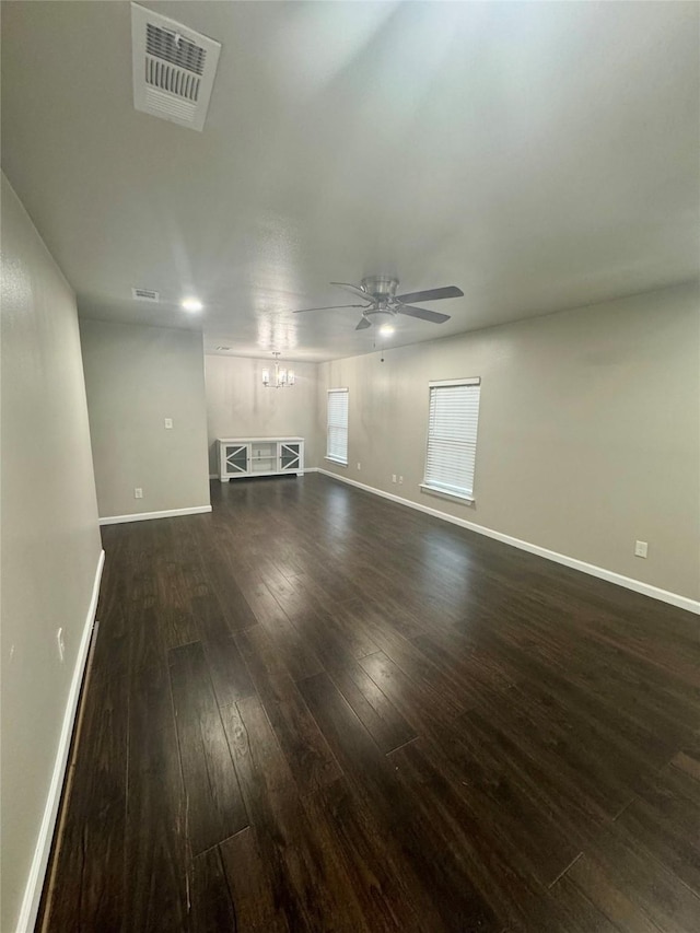 unfurnished living room with ceiling fan with notable chandelier and dark wood-type flooring