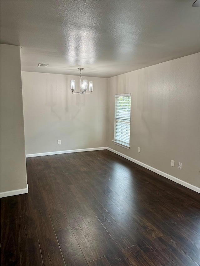 spare room with an inviting chandelier, dark wood-type flooring, and a textured ceiling