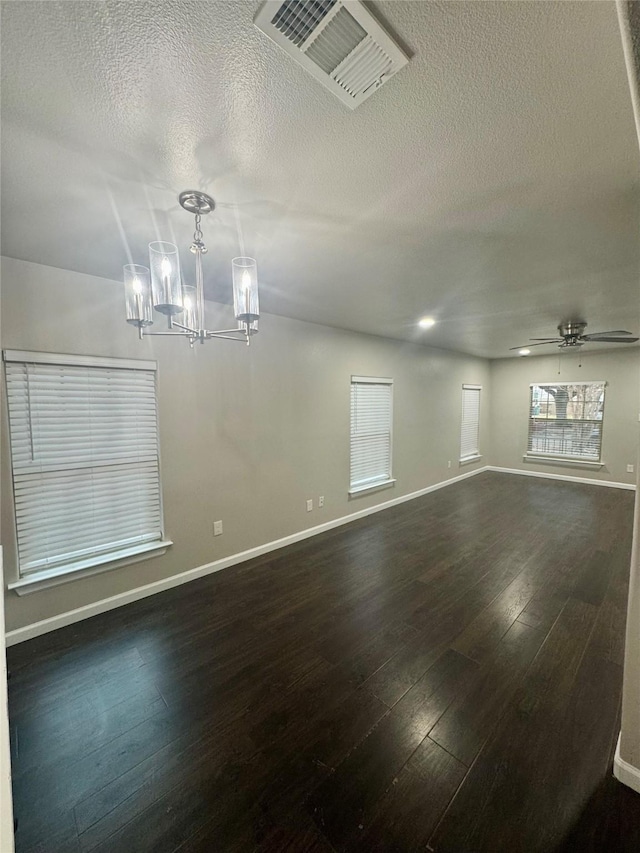 empty room with a healthy amount of sunlight, dark hardwood / wood-style floors, ceiling fan with notable chandelier, and a textured ceiling