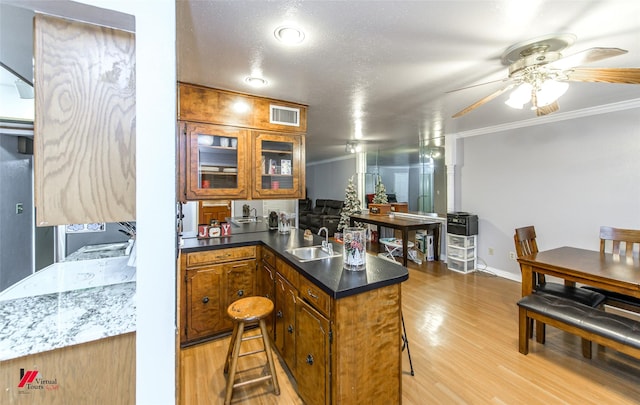 kitchen featuring sink, light hardwood / wood-style flooring, a kitchen breakfast bar, ornamental molding, and kitchen peninsula