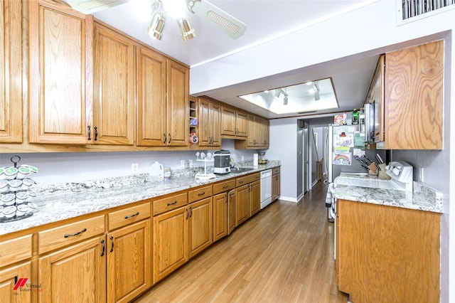 kitchen featuring light stone counters, light wood-type flooring, a tray ceiling, dishwasher, and ceiling fan