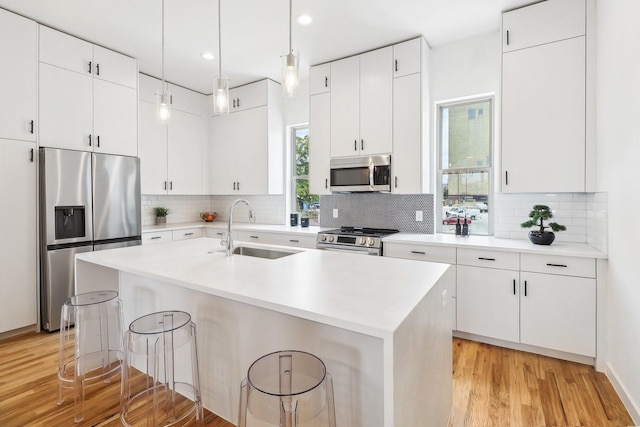 kitchen with appliances with stainless steel finishes, an island with sink, sink, white cabinets, and a kitchen bar