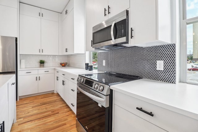 kitchen with stainless steel appliances, white cabinetry, backsplash, and light hardwood / wood-style flooring