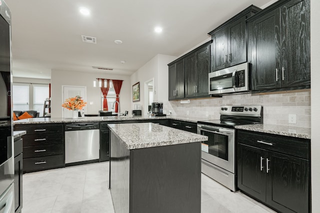 kitchen with a kitchen island, tasteful backsplash, kitchen peninsula, stainless steel appliances, and light stone countertops