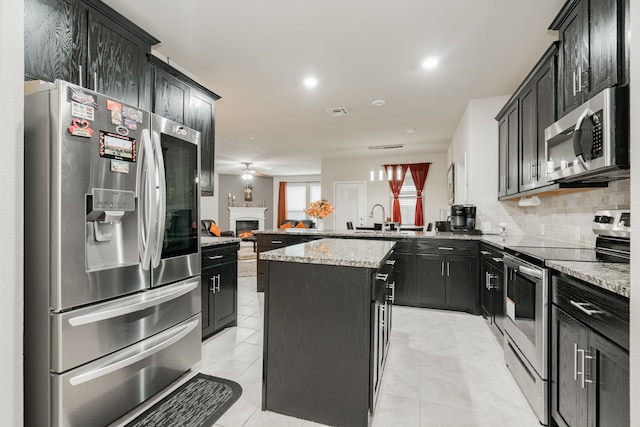 kitchen with backsplash, stainless steel appliances, a center island, light stone countertops, and kitchen peninsula